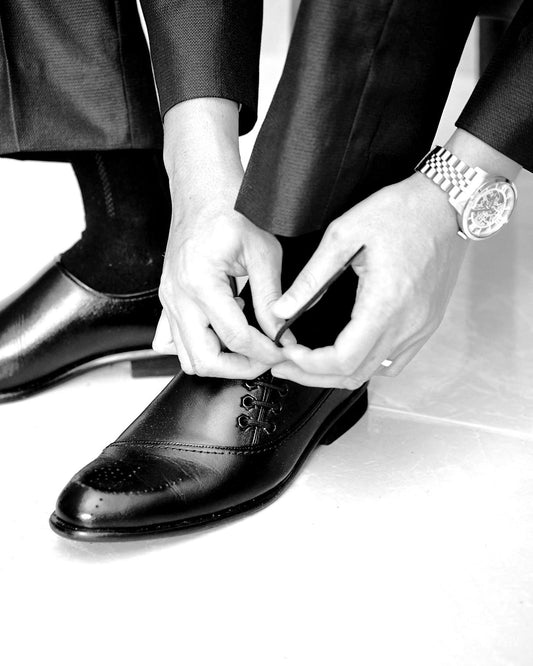 Editorial menswear — hands tying handcrafted leather oxford